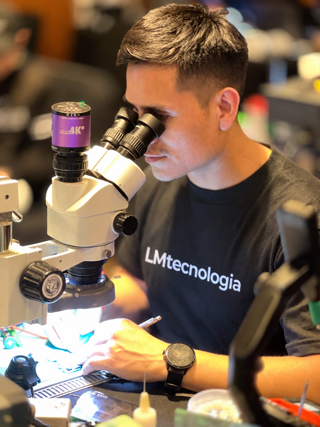 Luis, con remera de LMtecnología, trabajando con microscopio en la reparación de una placa
